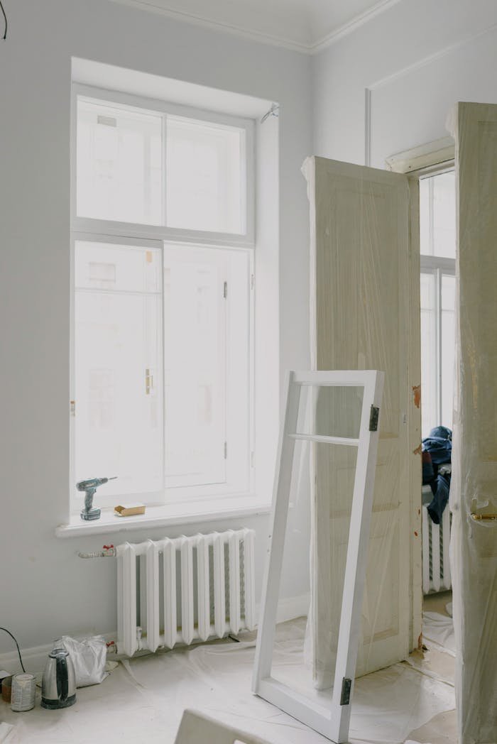 Bright room under renovation featuring white walls and windows, showcasing minimalist design.