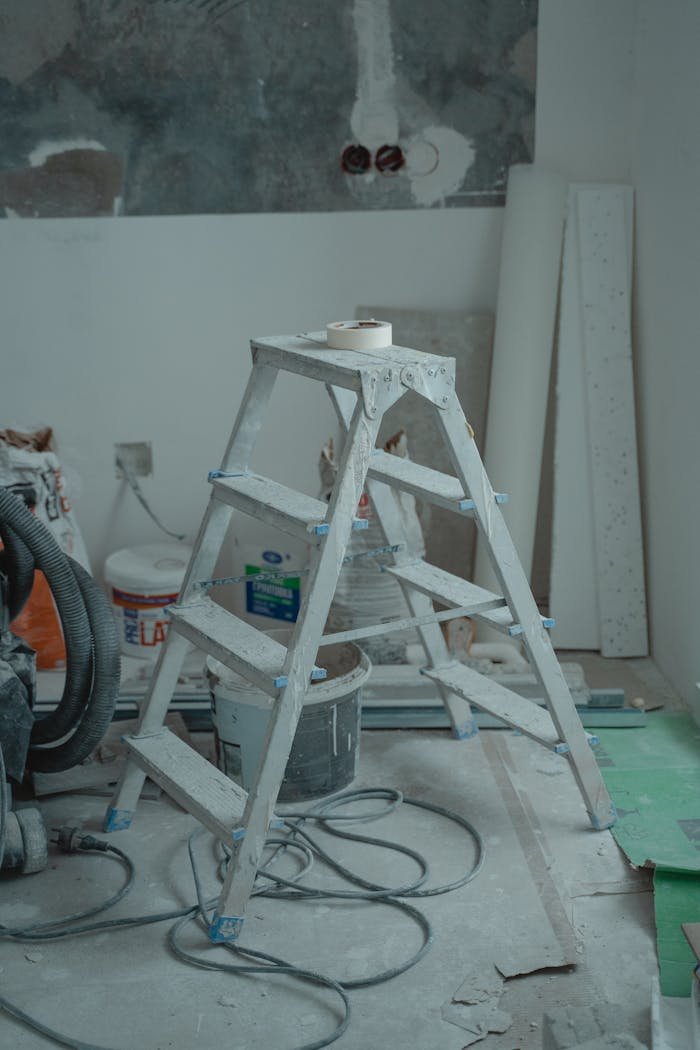 A metal ladder stands amidst renovation supplies including paints and plaster in an indoor setting.