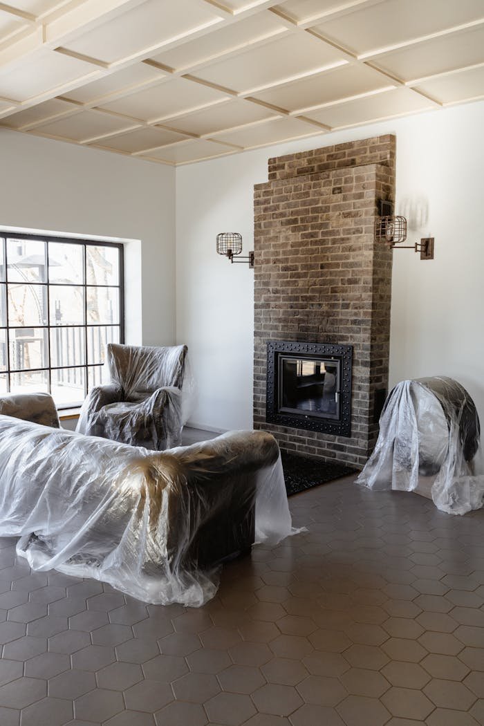 A cozy, modern living room with plastic-covered furniture and a brick fireplace under renovation.